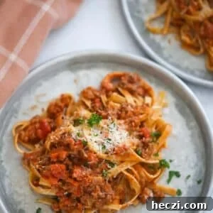two plates of fettuccine bolognese with a towel on the side.
