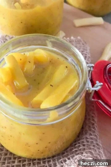 Homemade mustard pickles in a canning jar with a red lid, with another jar of mustard bean pickles in the background.