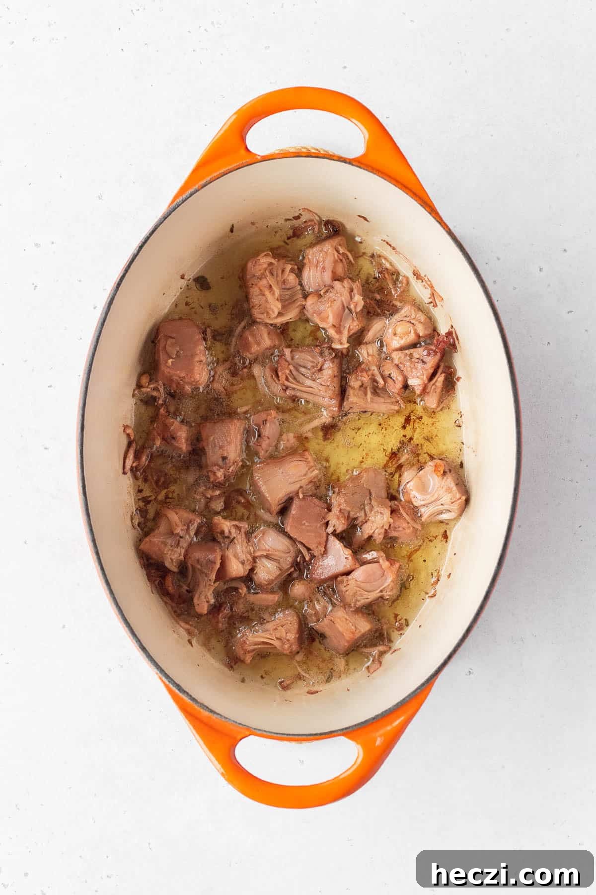 Young green jackfruit confit being cooked in oil in a pot.