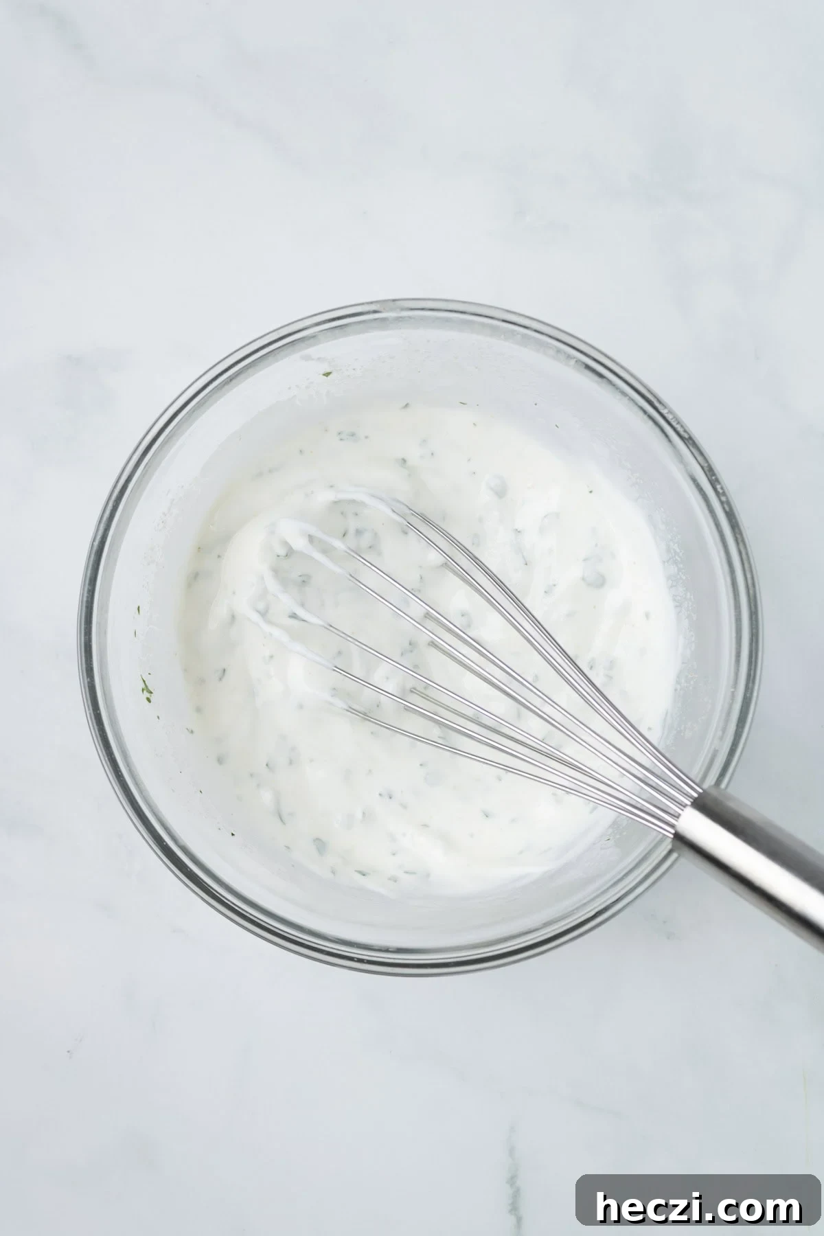 An overhead image of whisking the herbed yogurt sauce together in a bowl.