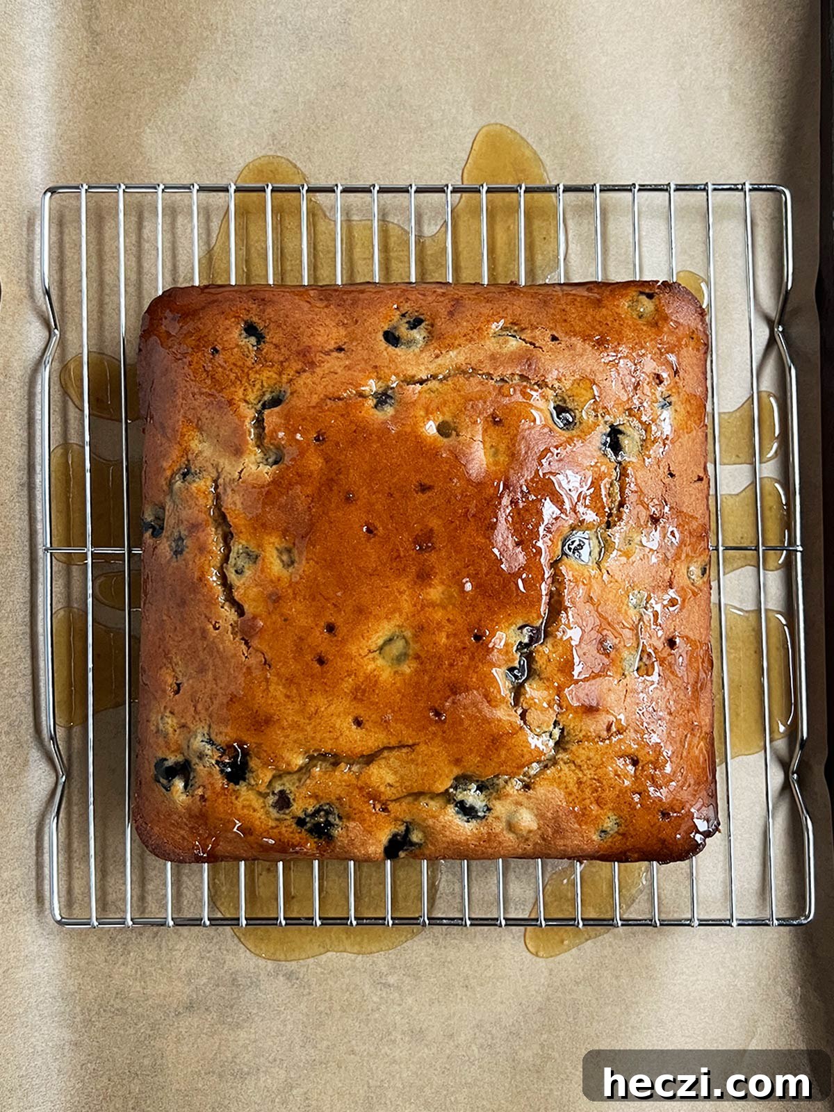 Olive oil blueberry cake on rack with glaze poured over and excess on the parchment paper below.