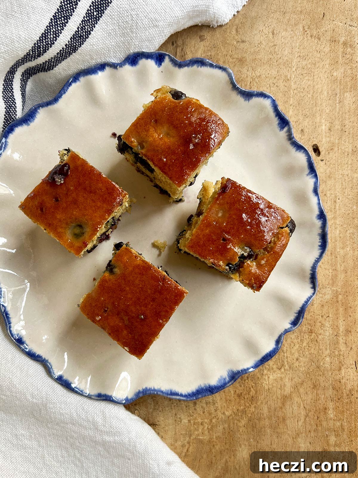 Four slices of blueberry cake on a blue-rimmed plate with a blue-lined napkin nearby.
