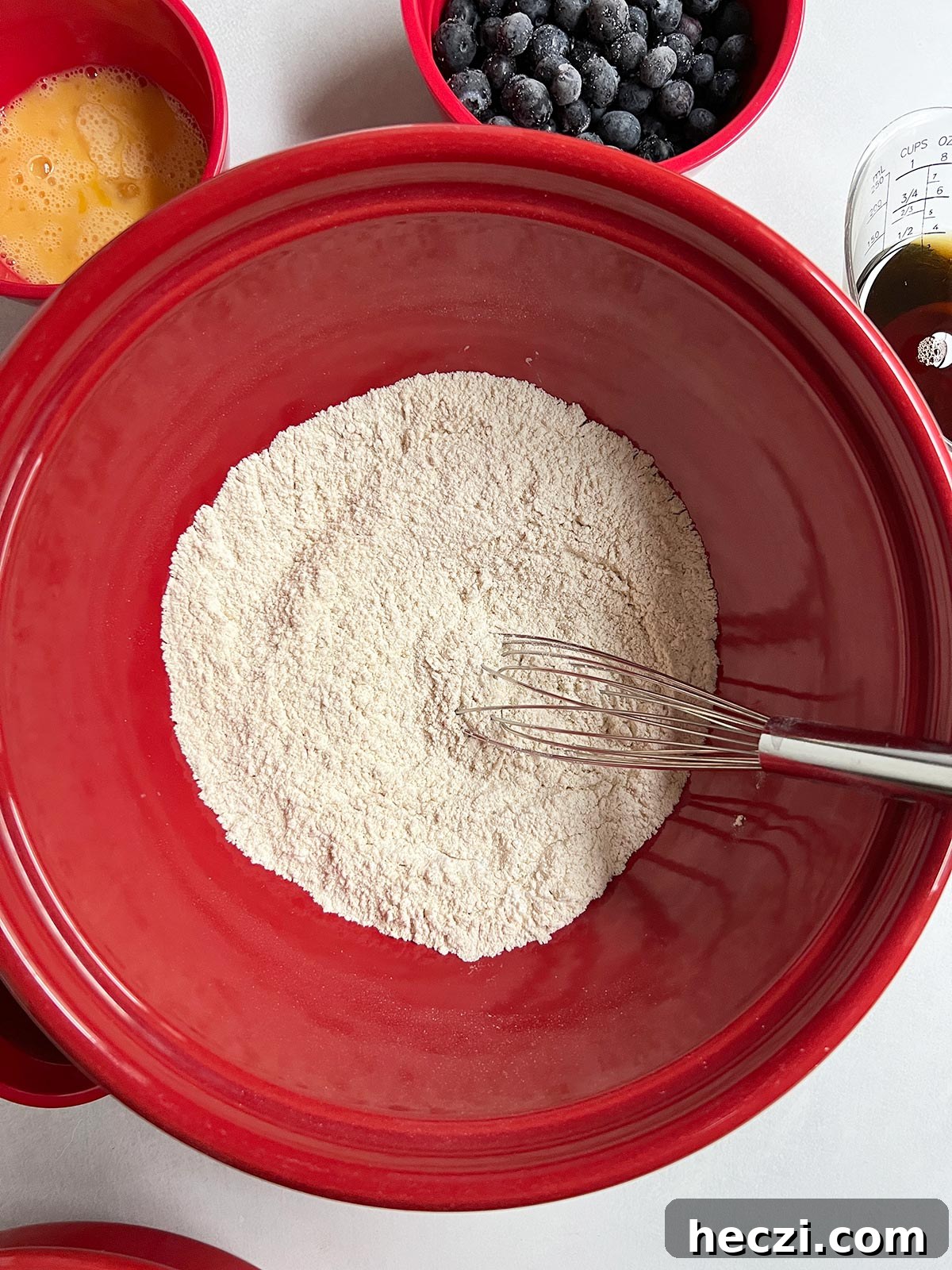 Dry ingredients for the blueberry breakfast cake in a big red bowl with a whisk.