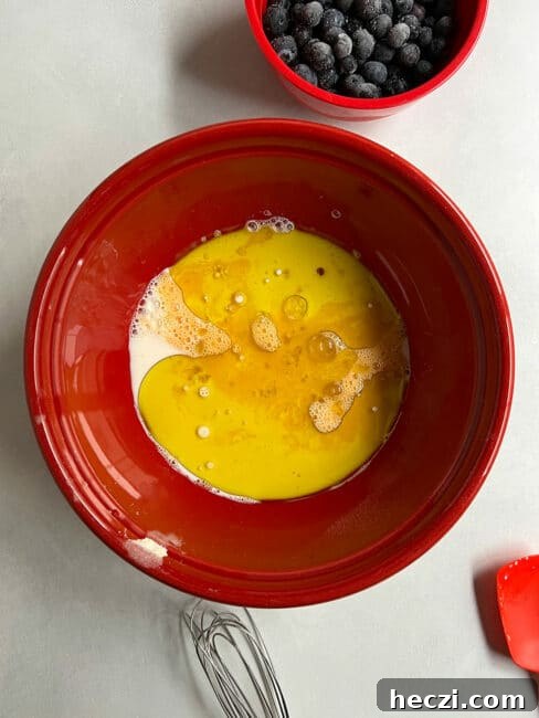 Wet ingredients for blueberry tea cake in a red bowl with a whisk nearby.