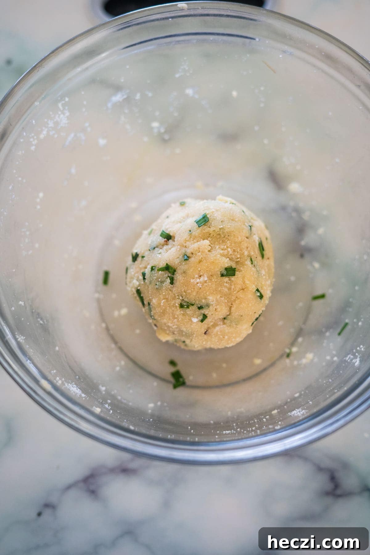 Cottage Cheese Crackers Recipe: Crispy Low-Carb Snack Guide 6 A ball of dough with chopped herbs is in a clear glass bowl on a marble surface.