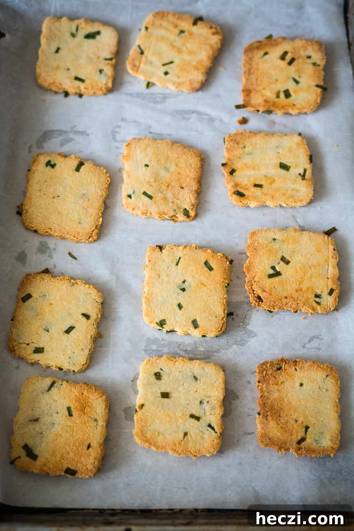 Cottage Cheese Crackers Recipe: Crispy Low-Carb Snack Guide 10 Twelve square, baked cookies with green herbs on a parchment-lined baking tray.