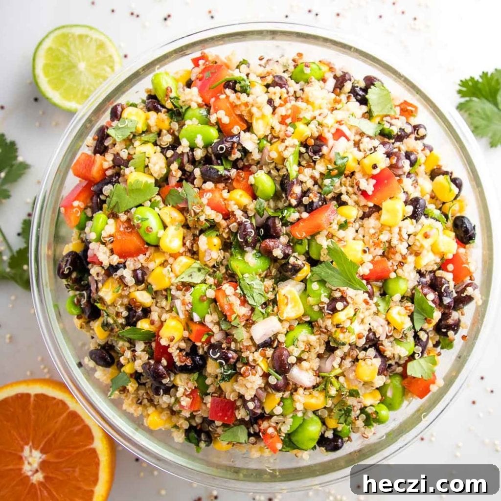 large glass bowl filled with colorful quinoa salad. half a lime, half an orange and fresh cilantro on the white counter surrounding the bowl. 