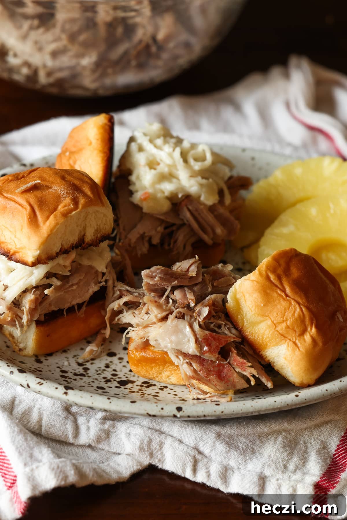 Pulled pork on a Hawaiian roll on a plate with pineapple slices