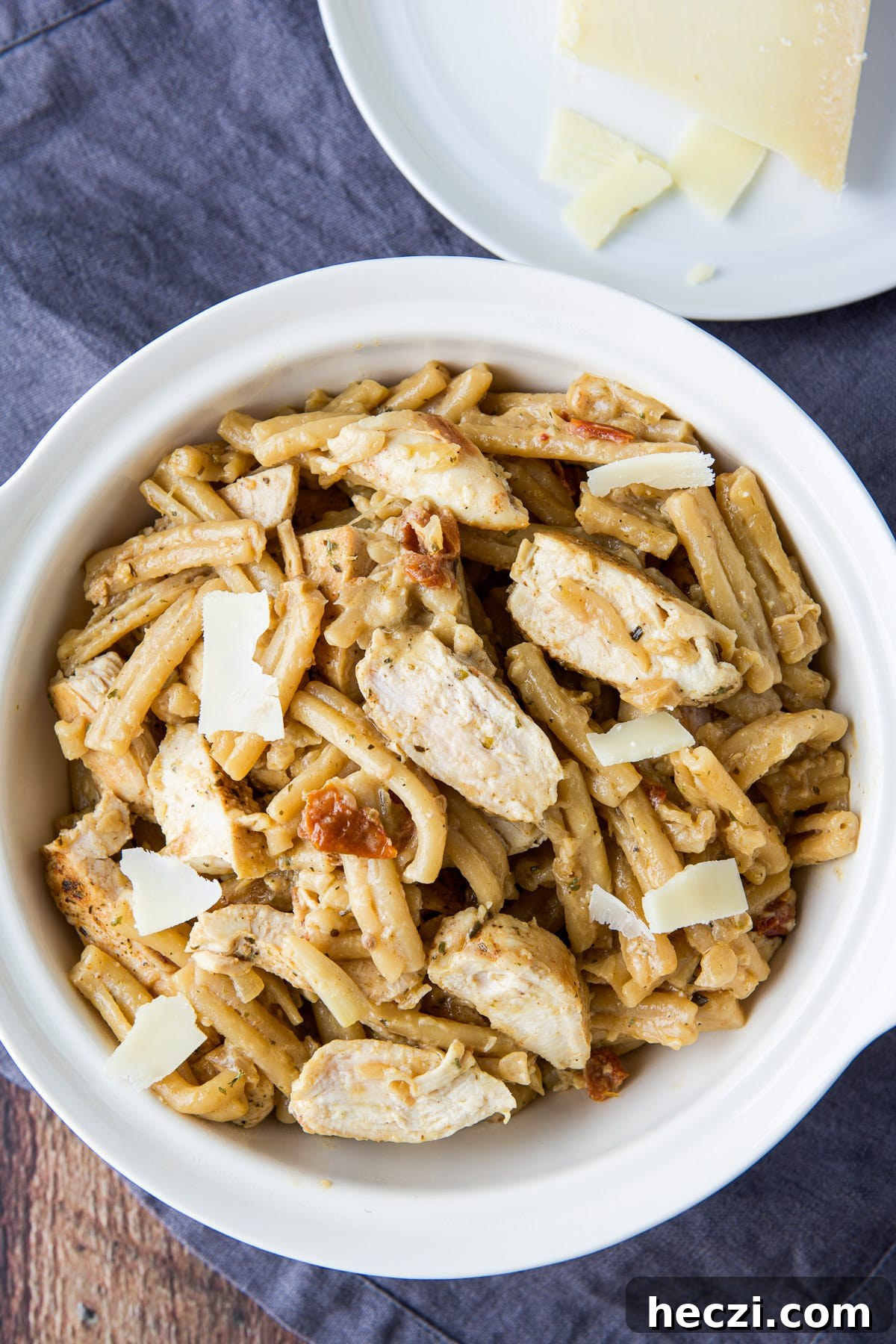 Overhead view of the bowl of pasta and chicken with a plate with cheese