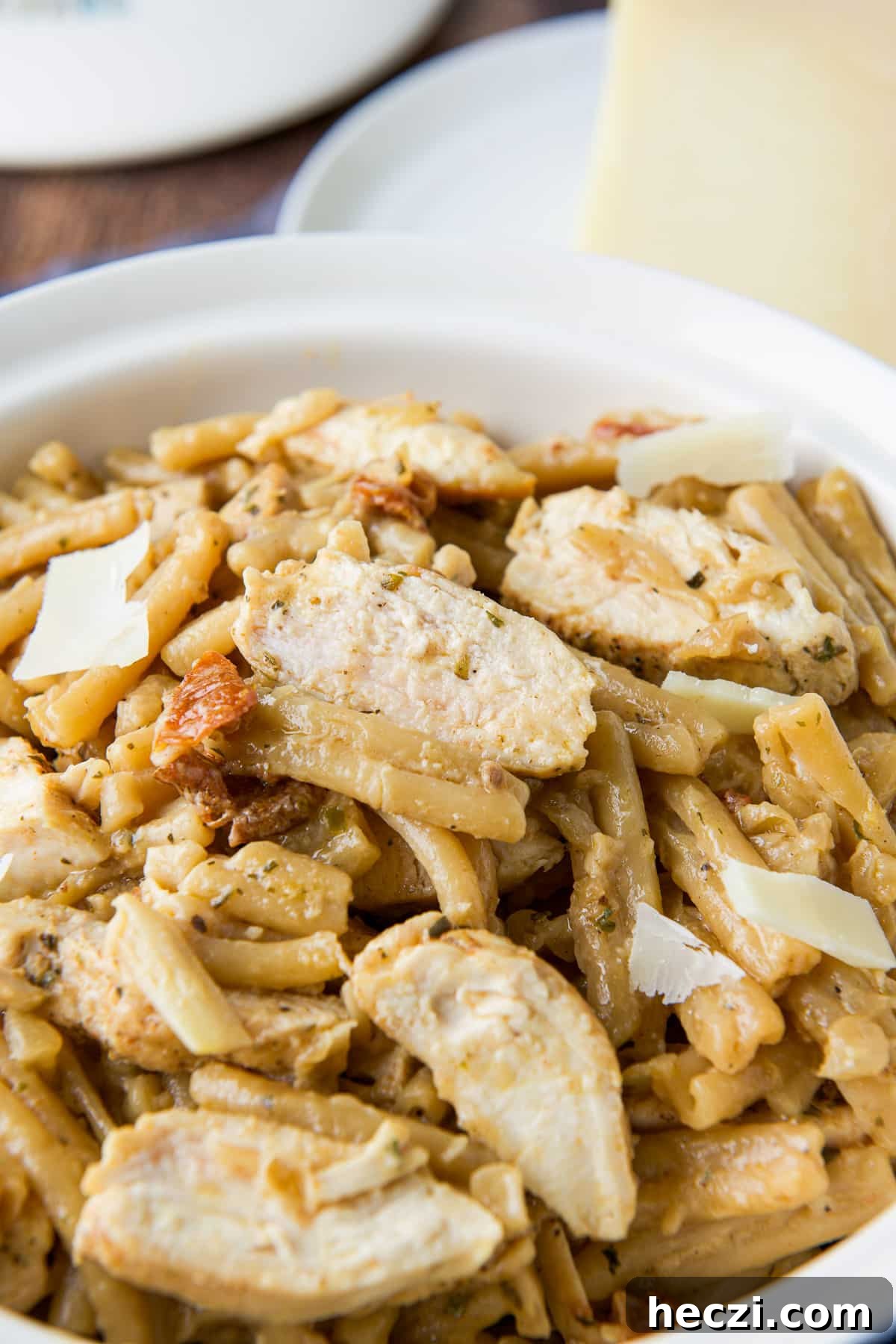 Sliced chicken on pasta with a sauce and cheese in the back