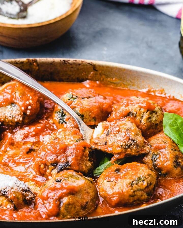 Eggplant Meatballs - sipandfeast.com #eggplantmeatballs #italianrecipes #eggplantrecipes Side angle view of eggplant meatballs in pan with grated Pecorino Romano in background.