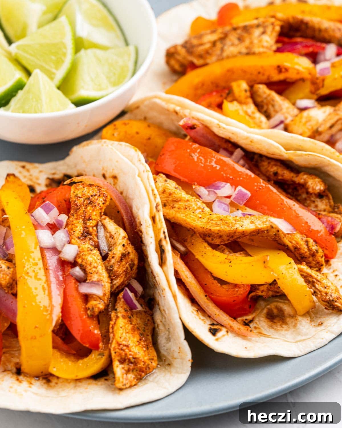close up plate of chicken fajitas tacos with lime wedges.