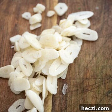 Homemade Italian Sunday Sauce Recipe for Classic Pasta Night 4 Garlic sliced thin on a cutting board.