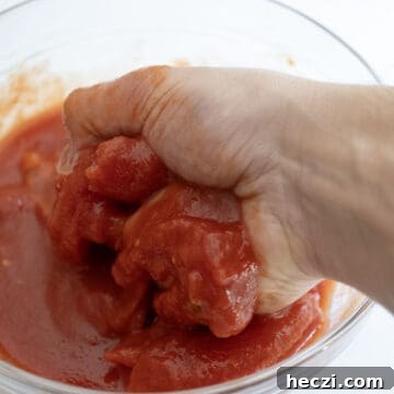 Homemade Italian Sunday Sauce Recipe for Classic Pasta Night 5 Hand crushing tomatoes in a bowl.