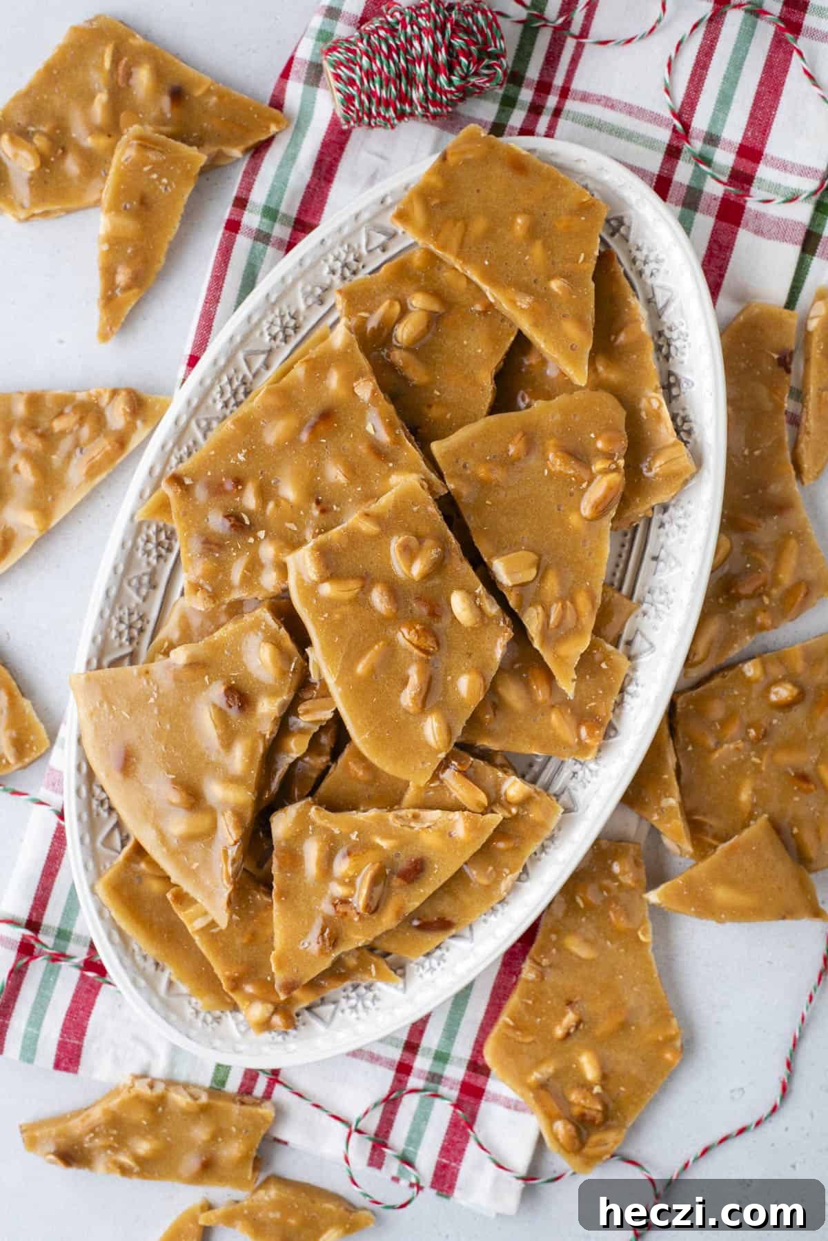 Classic Peanut Brittle Recipe: Crispy, Homemade Candy in 30 Minutes 2 a plate full of peanut brittle on top of a red and green plaid towel with more brittle spread around it