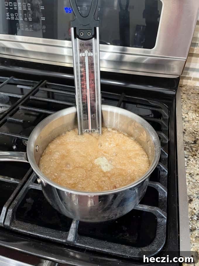Classic Peanut Brittle Recipe: Crispy, Homemade Candy in 30 Minutes 12 a pot on a stovetop with granulated sugar, water, corn syrup, baking soda, vanilla extract and peanuts cooking in it and a candy thermometer attached to the side