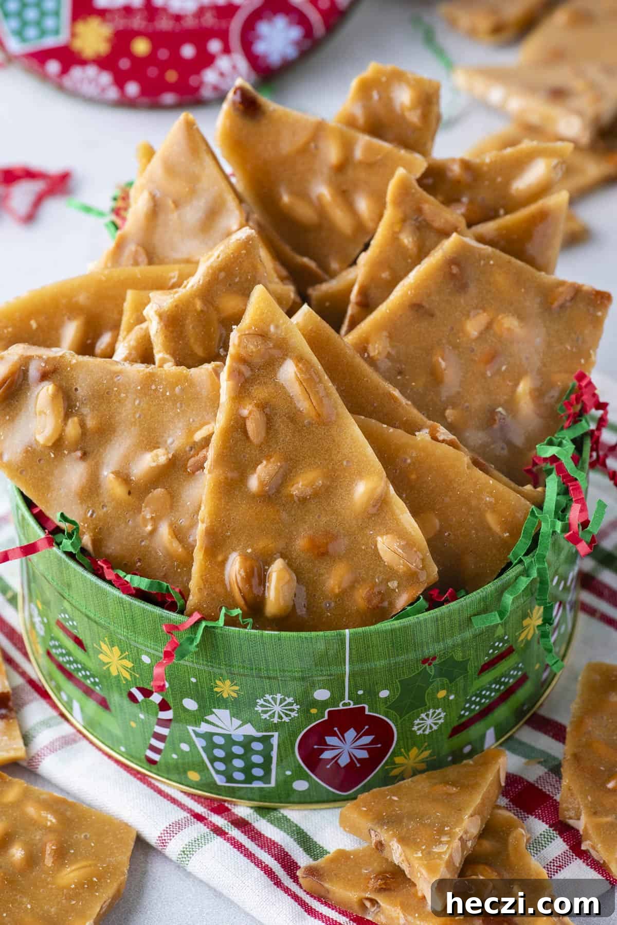 Classic Peanut Brittle Recipe: Crispy, Homemade Candy in 30 Minutes 17 a green Christmas container of peanut brittle with red and green christmas string and a red, green and white plaid towel underneath