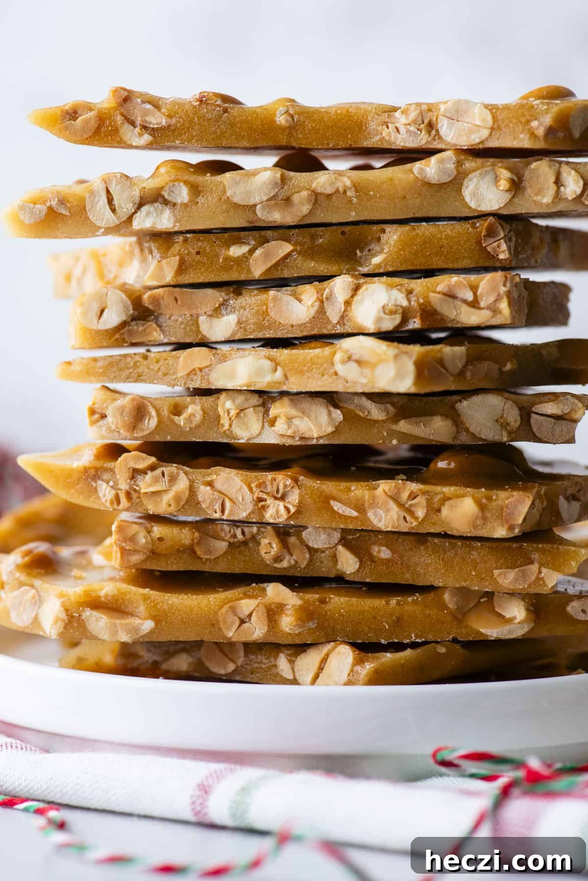 Classic Peanut Brittle Recipe: Crispy, Homemade Candy in 30 Minutes 3 a stack of peanut brittle on a white plate on top of a green green and white towel