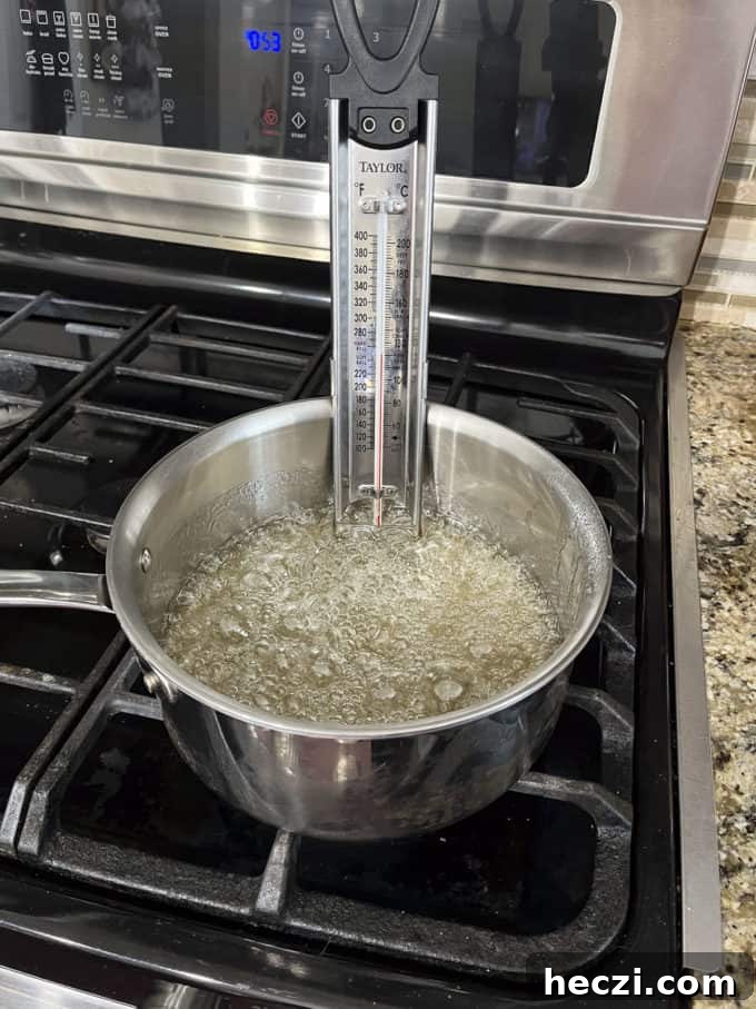 Classic Peanut Brittle Recipe: Crispy, Homemade Candy in 30 Minutes 9 a pot on a stovetop with granulated sugar, water and corn syrup cooking in it and candy thermometer attached to the side