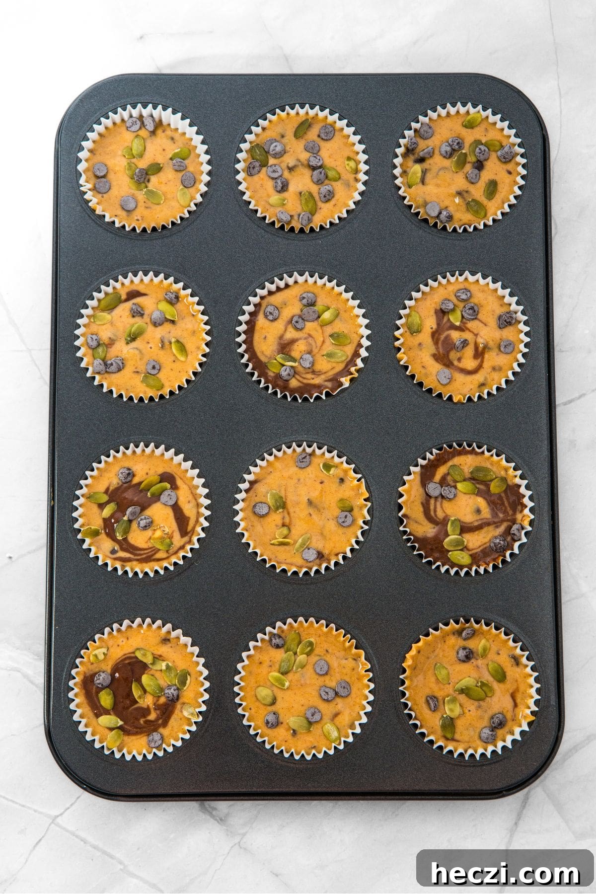 Pumpkin batter topped with pumpkin seeds in muffin pan.