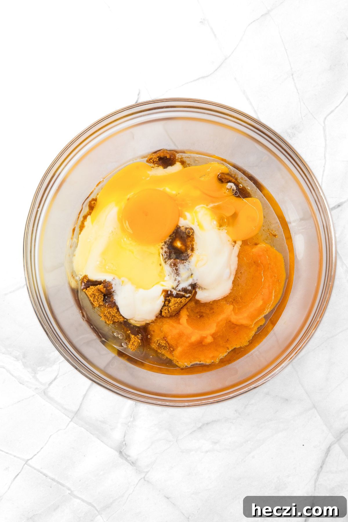 A glass bowl with pumpkin puree, sugar, oil, yogurt, eggs and vanilla extract.