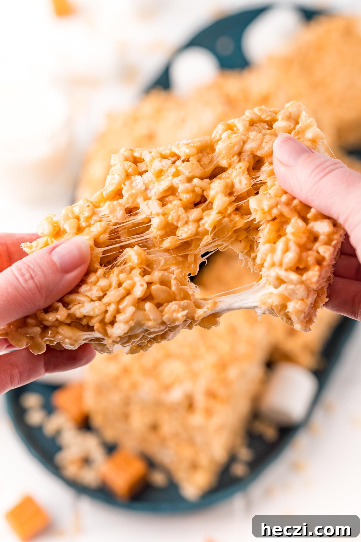 Caramel rice krispie treat being pulled apart by a woman's hands.