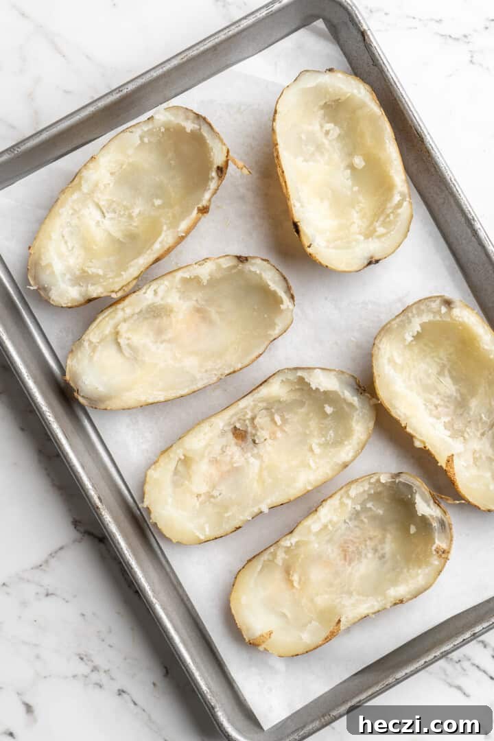 Hollow out the potatoes. Overhead view of hollowed out potato halves on baking sheet