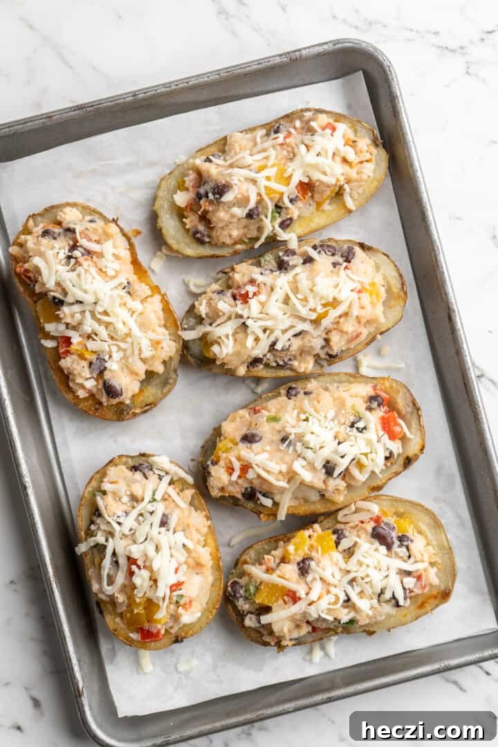 Fill the potato skins and bake. Overhead view of unbaked loaded potato skins on parchment-lined baking sheet