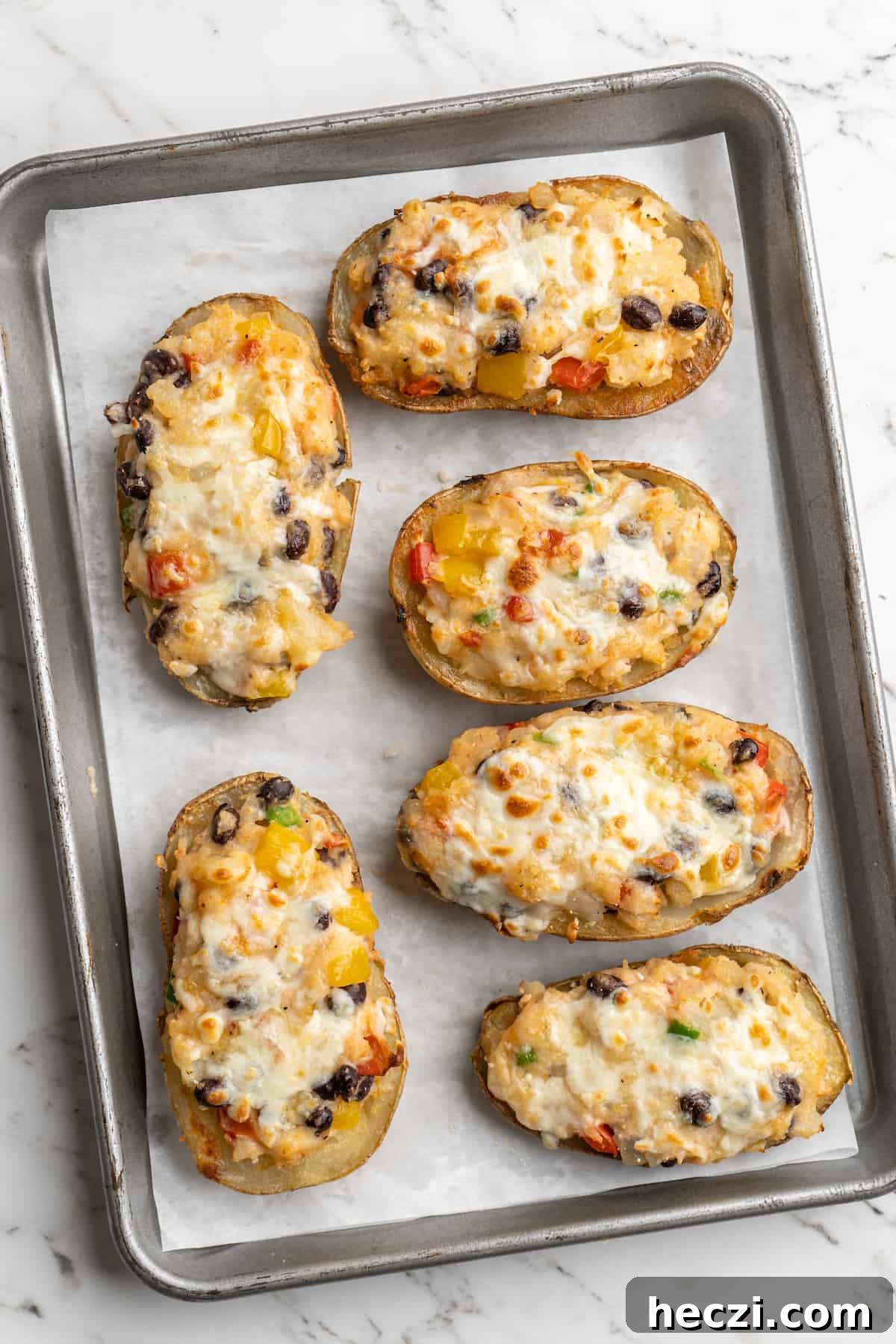 These crispy loaded potato skins are filled with veggies, black beans, vegan cheese, and sour cream. Overhead view of vegan loaded potato skins on parchment-lined baking sheet