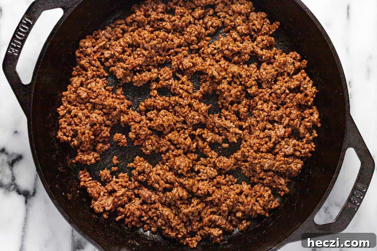 Creamy Rotel Dip Recipe with Cheesy Sausage for Parties 4 Cast iron skillet filled with browned ground beef seasoned with taco seasoning.