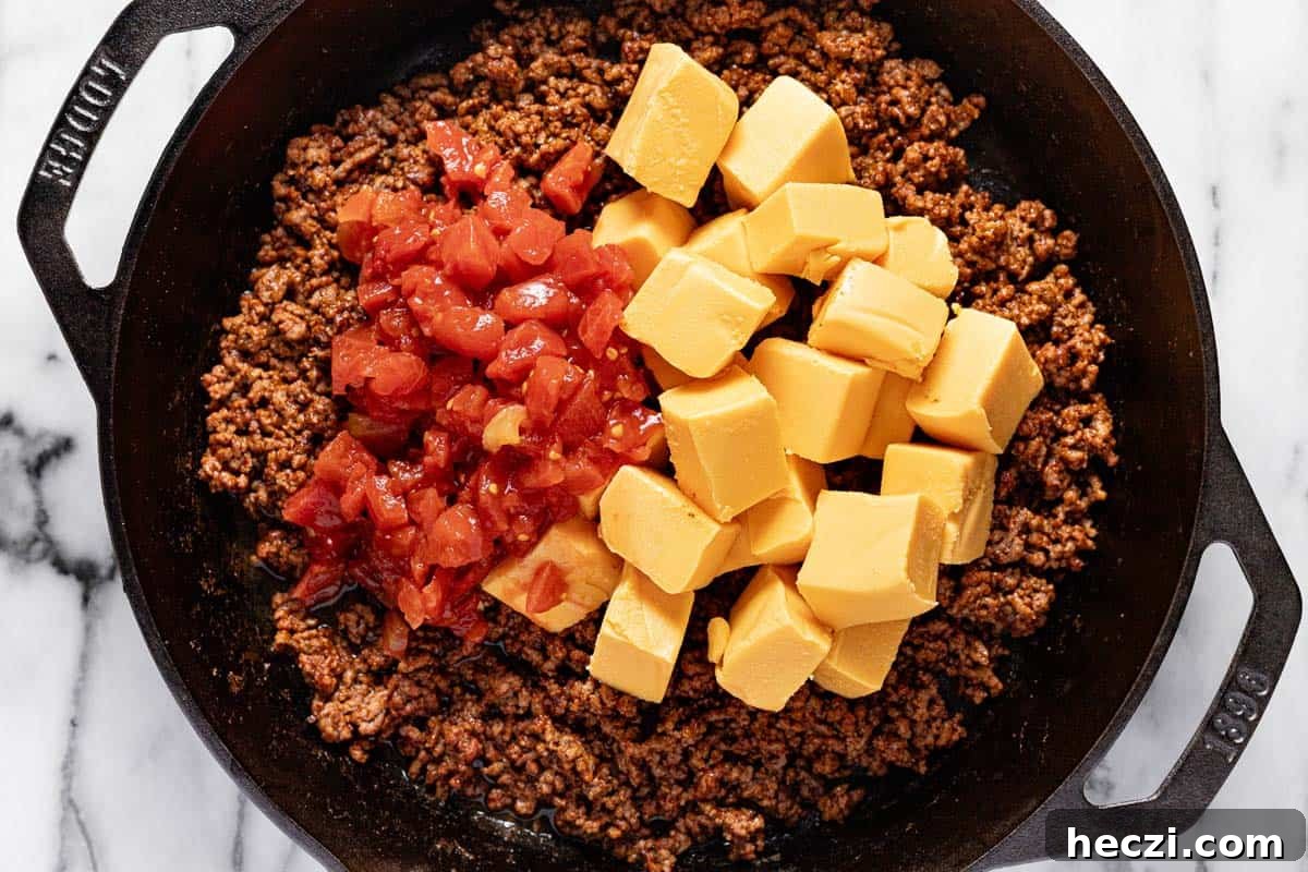 Creamy Rotel Dip Recipe with Cheesy Sausage for Parties 5 Cast iron skilled with taco meat, Rotel tomatoes, and diced Velveeta cheese.
