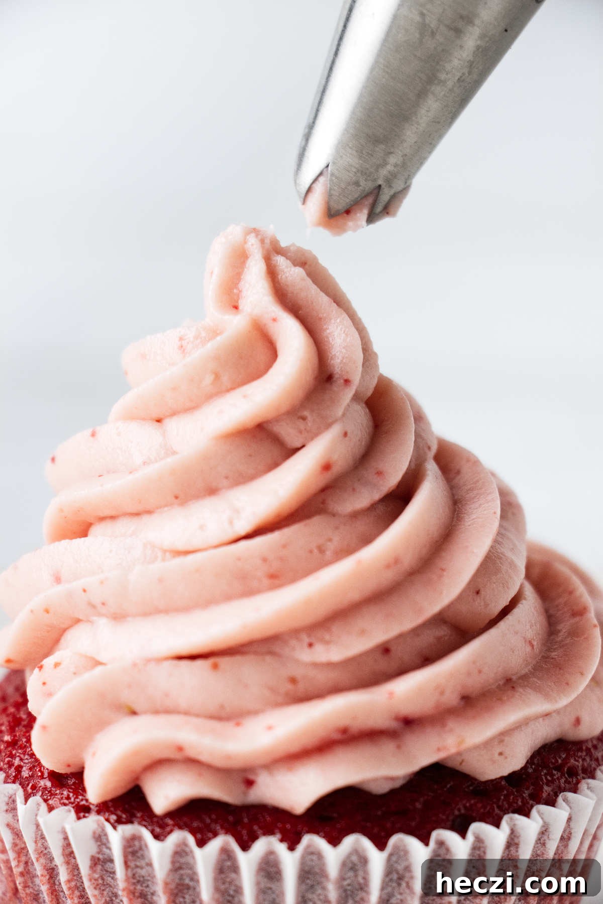 Strawberry Cream Cheese Frosting Recipe for Cakes & Cupcakes 5 Piping strawberry frosting on a cupcake.