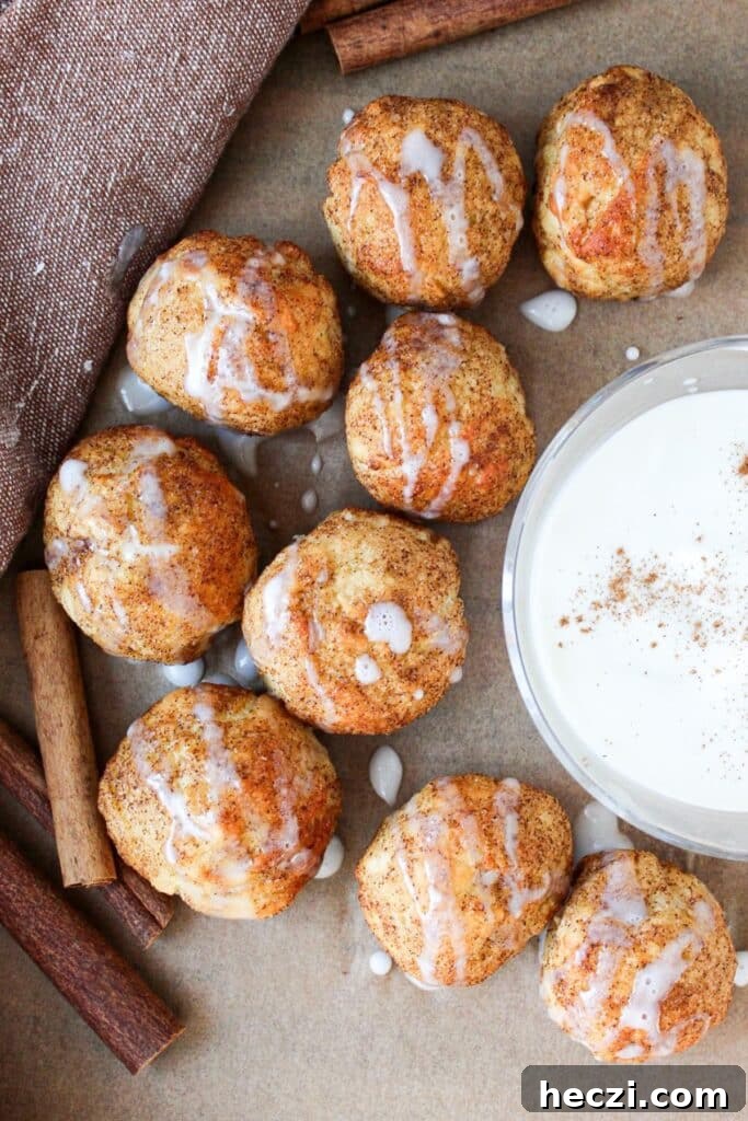 Air Fryer Cinnamon Roll Bites Made with 2-Ingredient Dough 2 Cinnamon roll bites on parchment paper with a greek yogurt glaze dip.