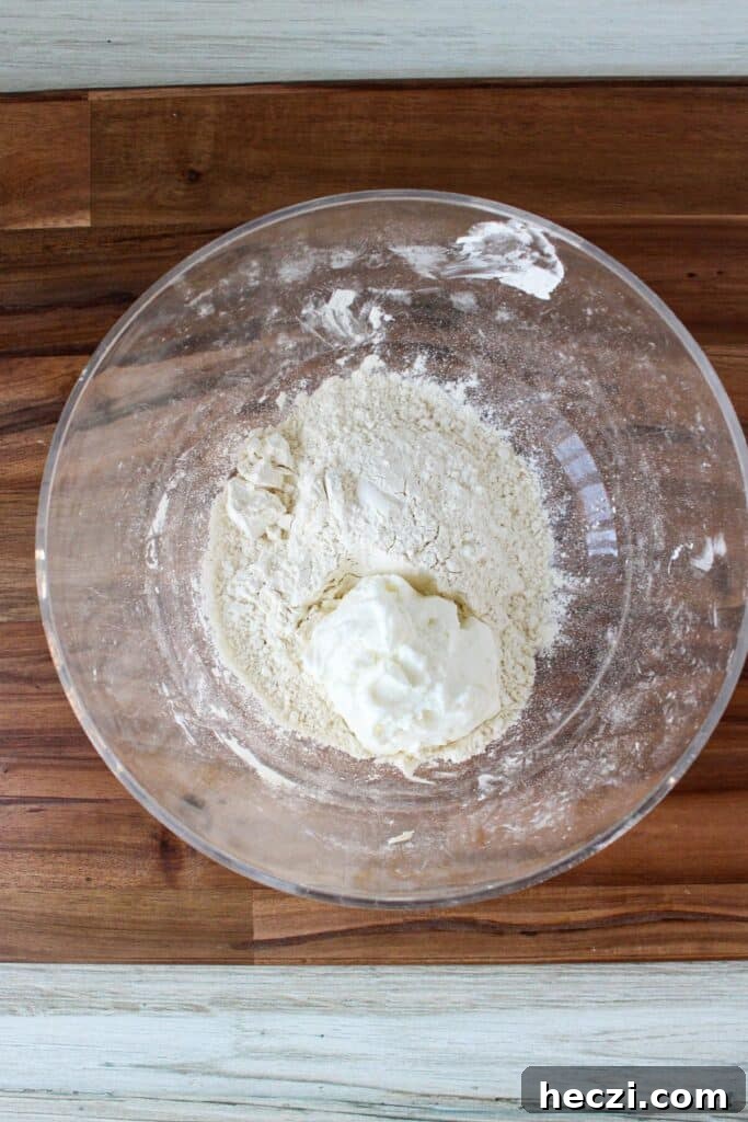 Air Fryer Cinnamon Roll Bites Made with 2-Ingredient Dough 4 A clear bowl of self rising flour and Greek yogurt.