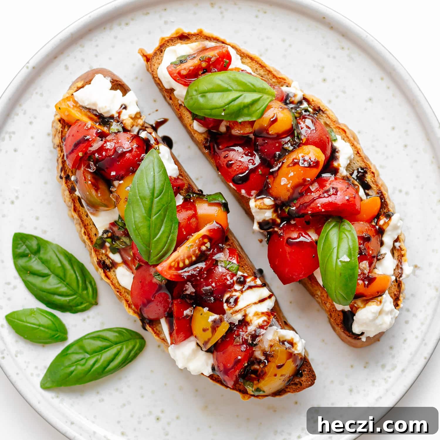 Two pieces burrata bruschetta with marinated tomato basil topping on a plate.