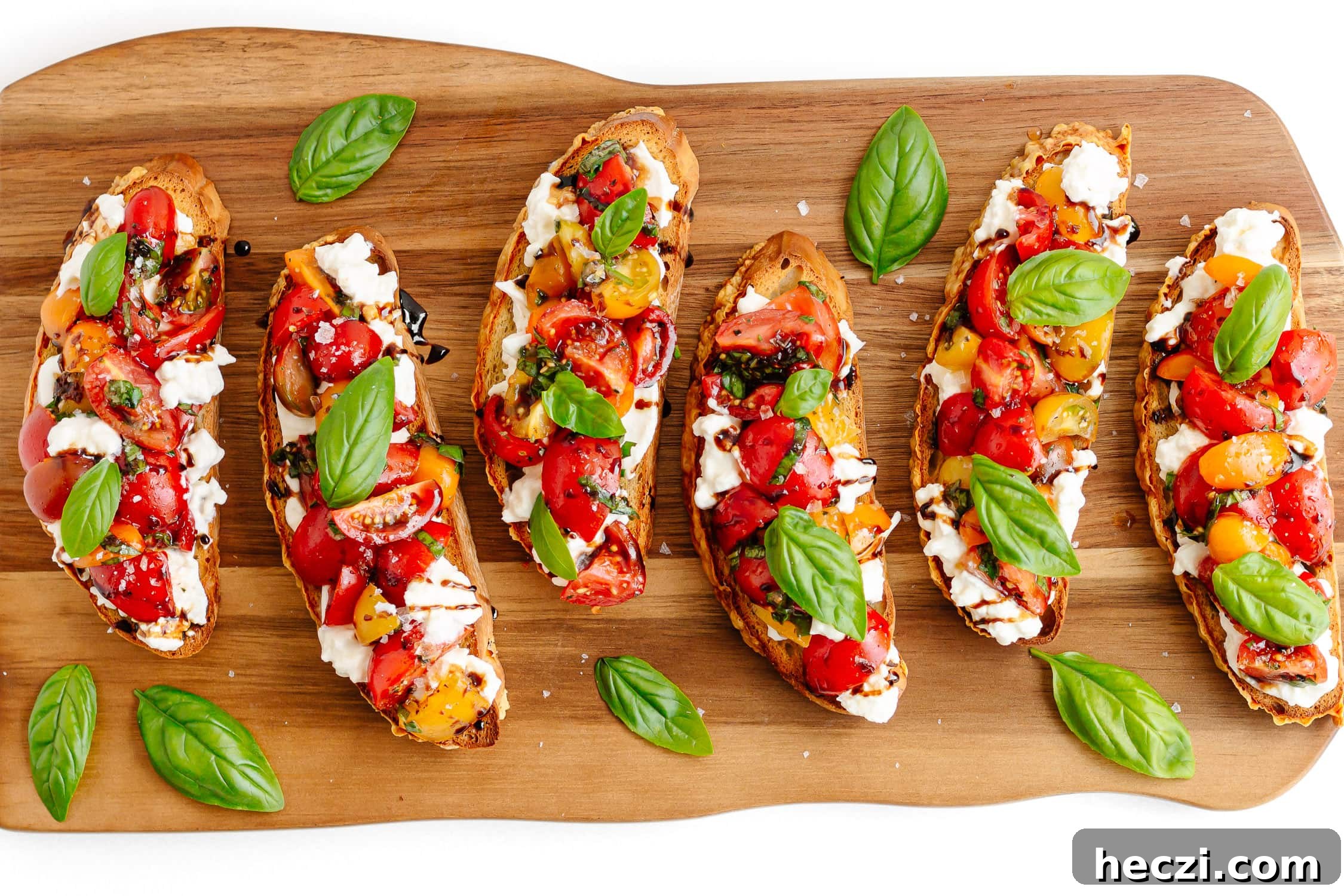 Burrata bruschetta with tomato and basil topping arranged on a wooden serving board.
