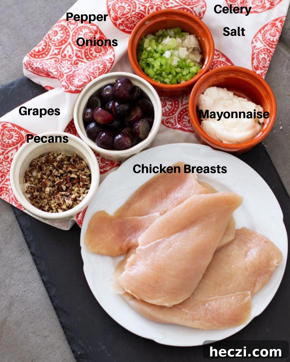 Ingredients on a black serving tray including chicken breast, celery, onion, red grapes, mayonnaise and pecans.