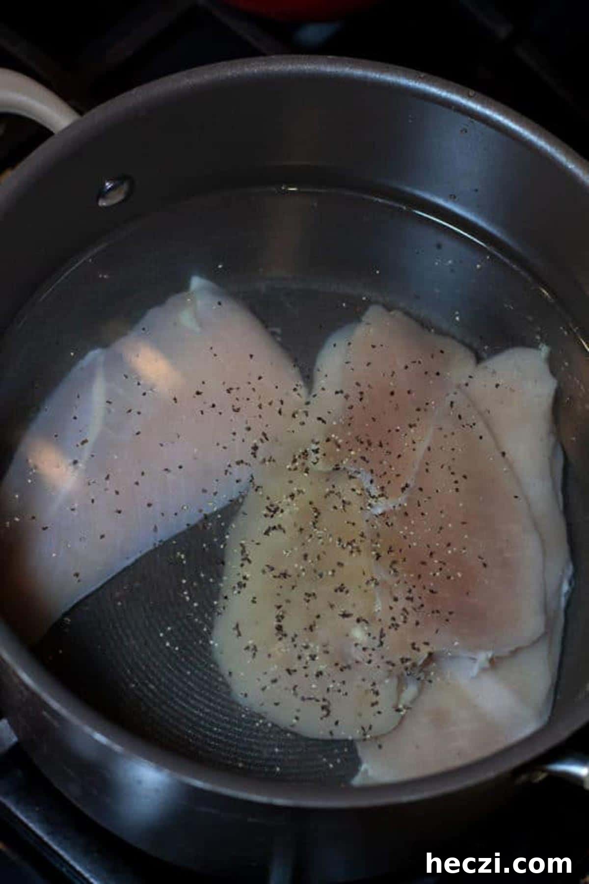 Large pot containing raw chicken being brought to a boil, pinch of salt and pepper in water.