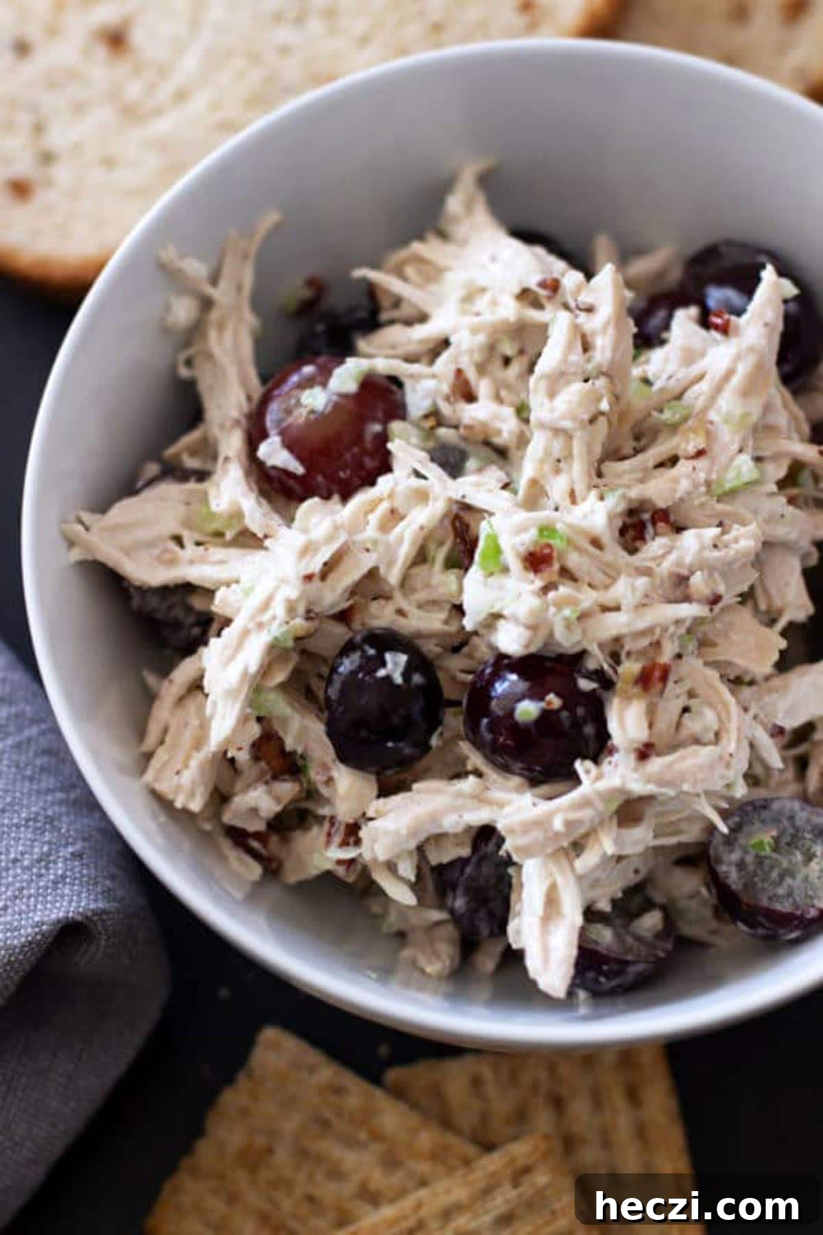 White bowl containing chicken salad topped with red grapes, crackers on table.