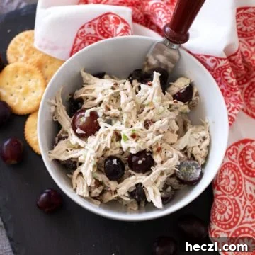 White bowl of chicken salad on a black serving tray, bread, crackers and grapes on serving dish.