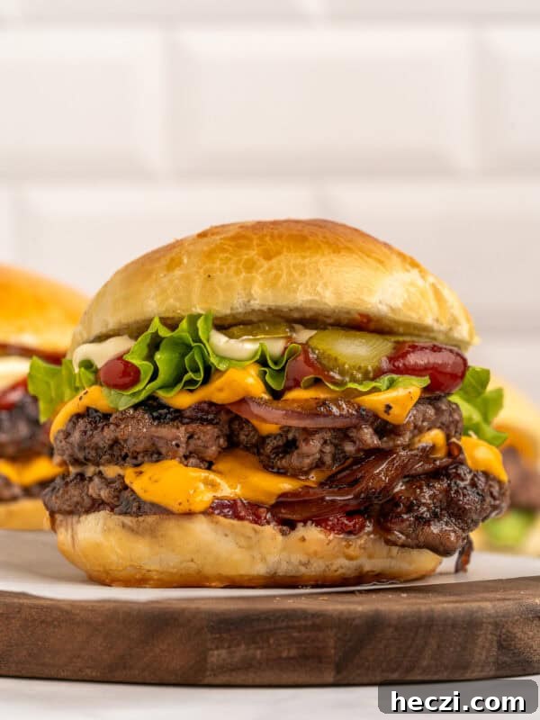 How to Make a Crispy Smash Burger at Home 8 A double cheeseburger with two beef patties, cheddar cheese, lettuce, pickles, ketchup, mayonnaise, and grilled onions in a brioche bun, served on a wooden board.