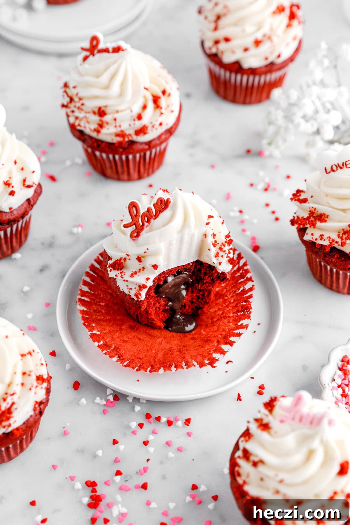 Red Velvet Molten Lava Cupcakes: Gooey Chocolate Center Delight 5 A red velvet lava cupcake sits on a white plate with its wrapper fully peeled back, revealing a gooey molten chocolate center. The cupcake is topped with a swirl of cream cheese frosting, red velvet crumbs, and a red