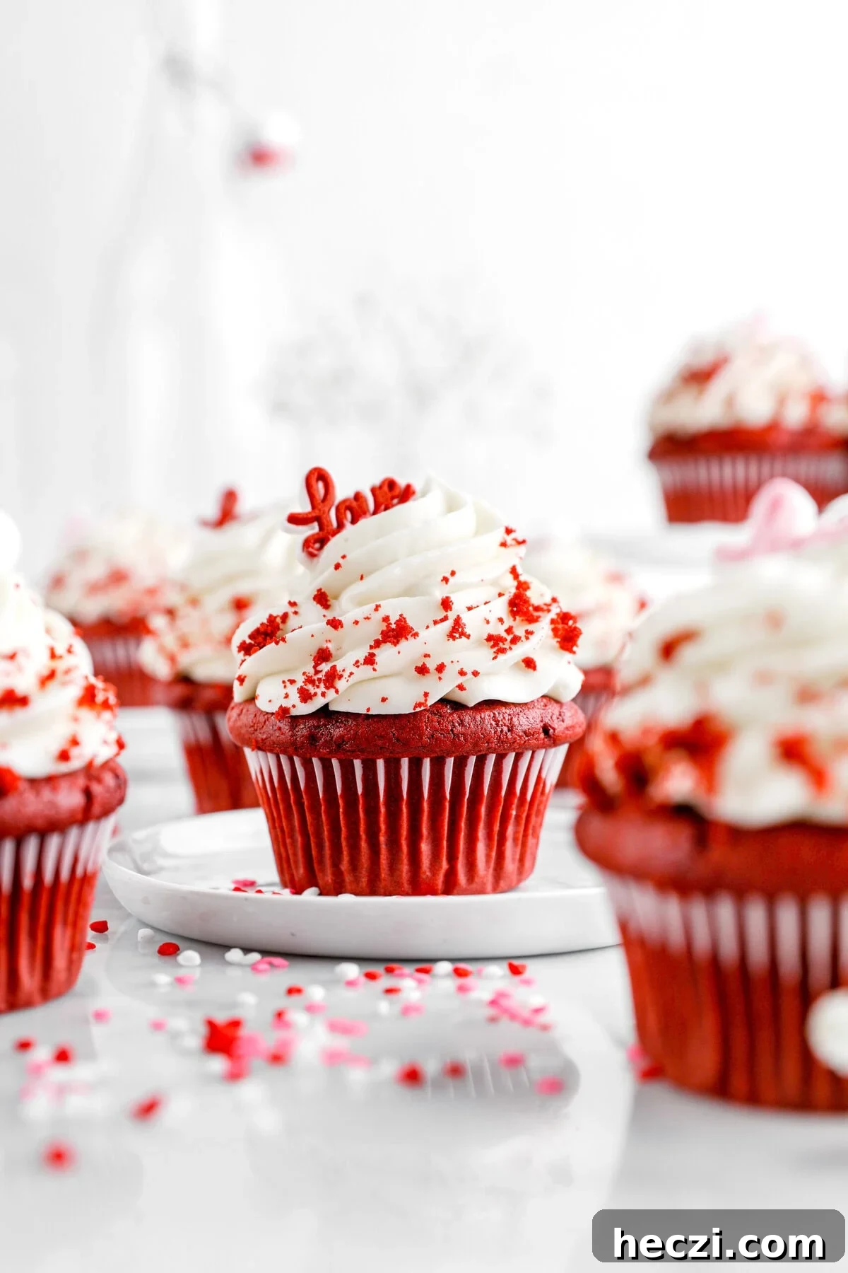 Red Velvet Molten Lava Cupcakes: Gooey Chocolate Center Delight 10 A red velvet cupcake with a deep red hue sits on a white plate, topped with a swirl of white frosting and sprinkled with red velvet crumbs. A small red 'Love' topper is nestled into the frosting.