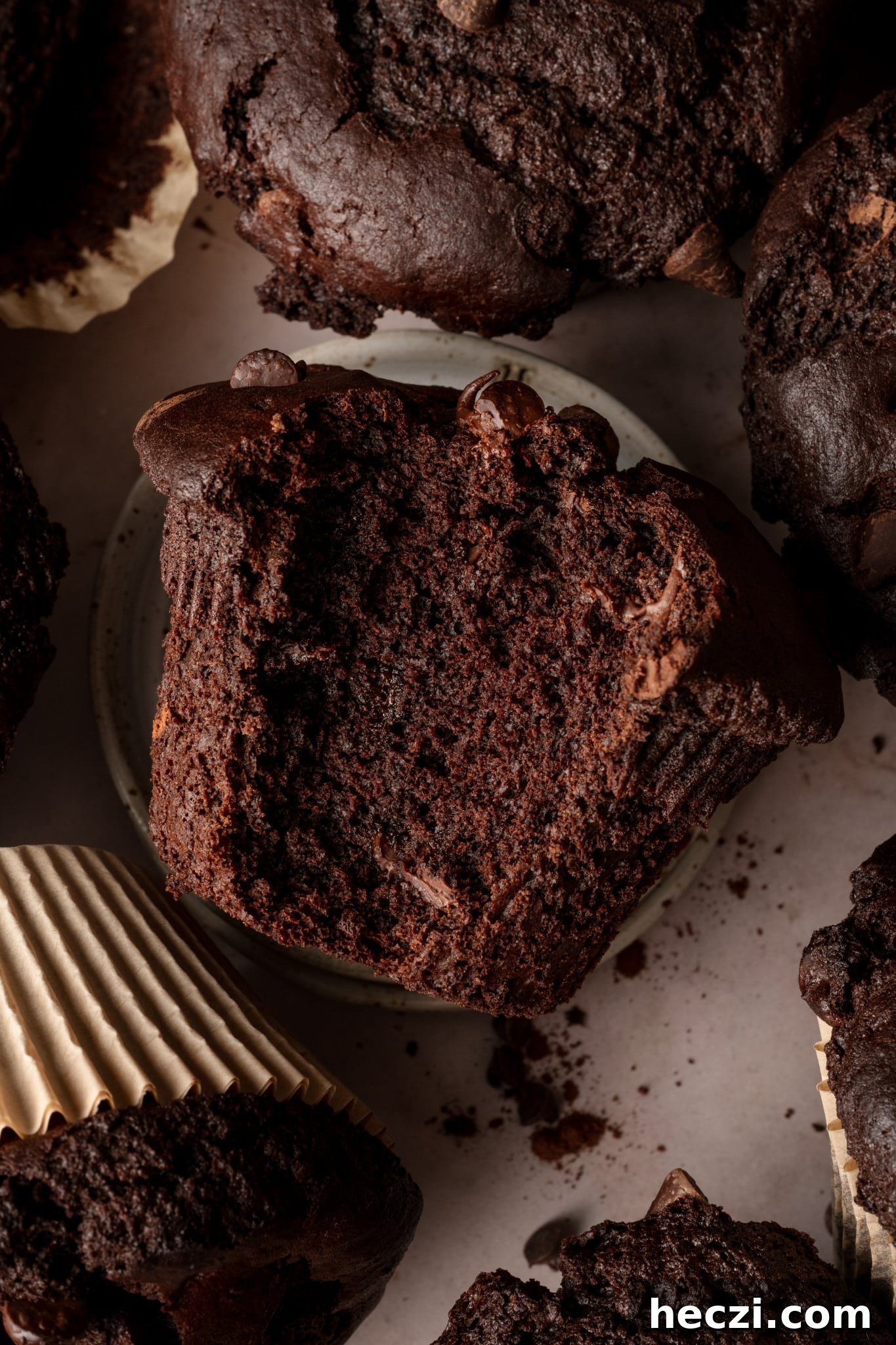 Costco-Style Double Chocolate Muffins Recipe (Copycat) 6 Large, bakery-style chocolate muffin on plate with bite taken out of the middle and the rest of the muffins surrounding it.