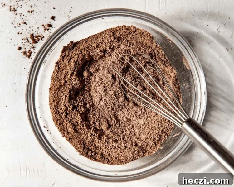 Dry ingredients for double chocolate muffins whisked together in clear mixing bowl with whisk.