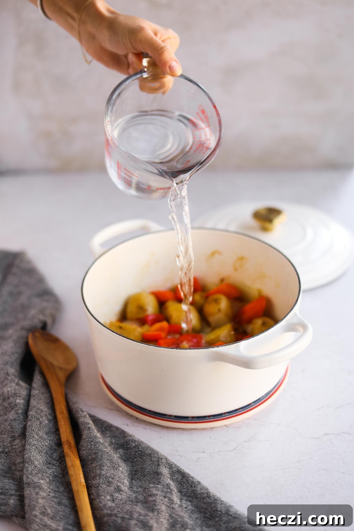 Japanese Chicken Katsu Curry Recipe — Crispy Cutlet with Rich Curry 6 Measuring cup pouring water on onion, potatoes, and bell peppers in white Le Creuset dutch oven with wooden spoon