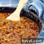 Bourbon Bacon Grilled Baked Beans in a cast iron skillet with a wooden spoon and blue towel