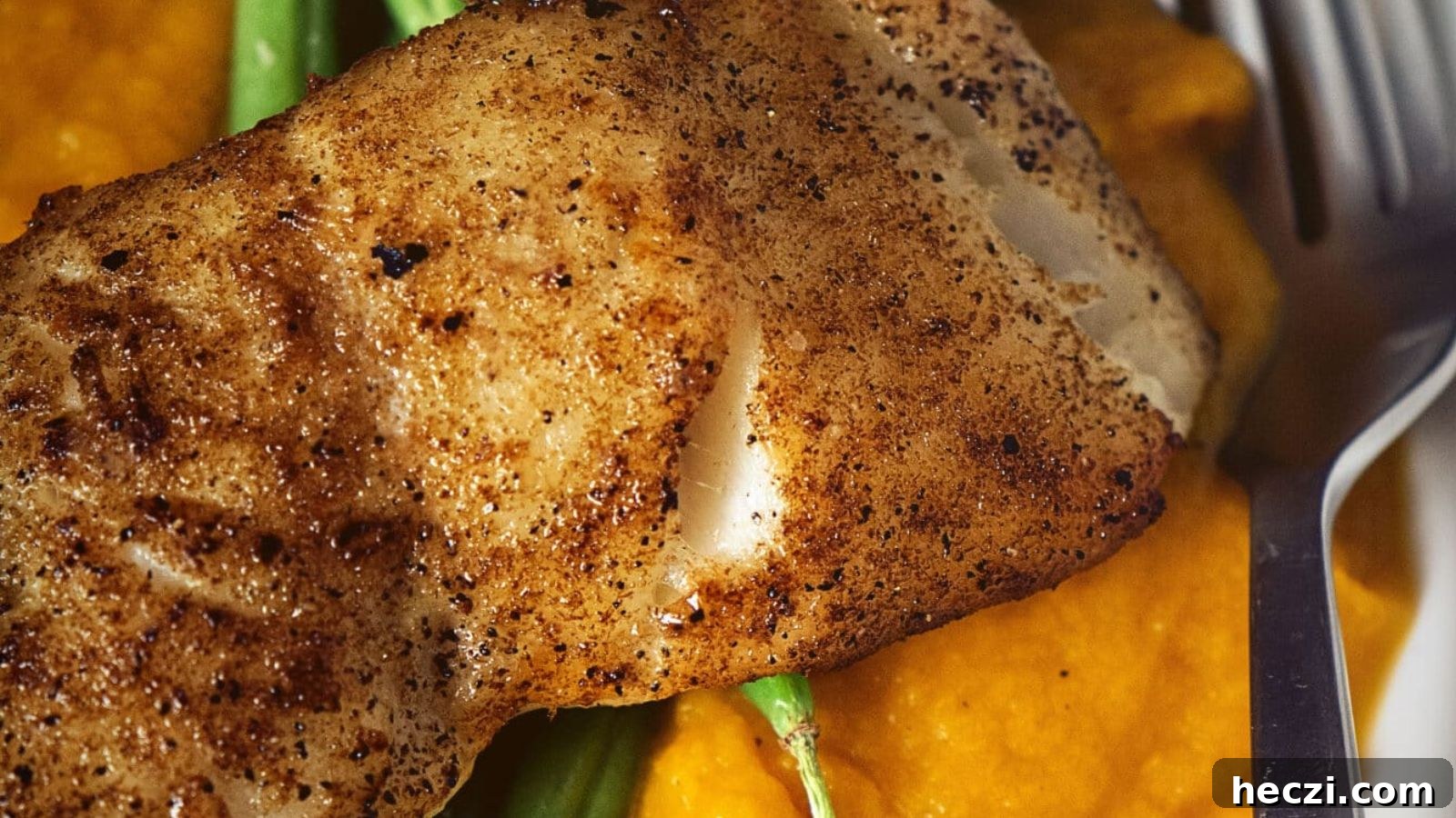 Pan-seared Chilean sea bass with browned edges topped with lemon and herbs on white plate.