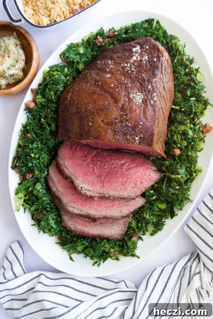 Perfect Picanha Roast Recipe for Juicy, Crispy Crust 2 a half-sliced Picanha Roast on top of sauteed greens surrounded by other side dishes before serving