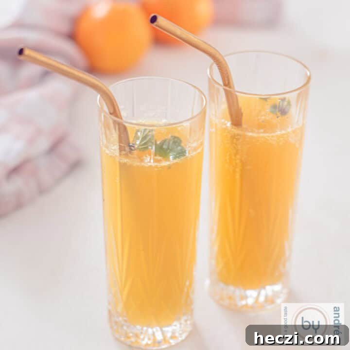 A square photo of two glasses with mandarin champagne cocktail a golden straw. Two mandarins in the background.